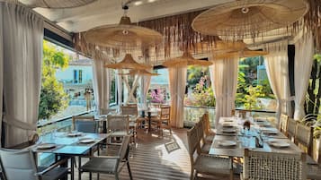 Un restaurante con mesas al aire libre, muebles de mimbre y sombrillas colgantes de ratán.