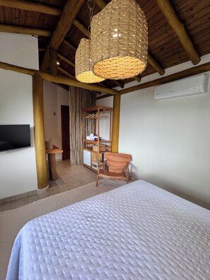 Un dormitorio con una cama, una silla de madera, un televisor, un armario y una lámpara colgante.