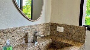A bathroom with a granite countertop, a round mirror, a faucet, and a soap dispenser.
