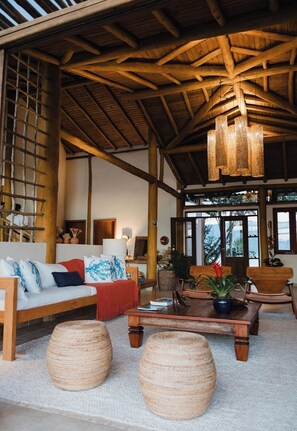 A spacious room with a high wooden ceiling, a sofa set, a coffee table, and large woven stools. - Luxury suite with a magnificent sunset view. (São Sebastião)