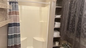 Une salle de bain avec une douche, un porte-serviettes et une étagère où sont pliés les serviettes.