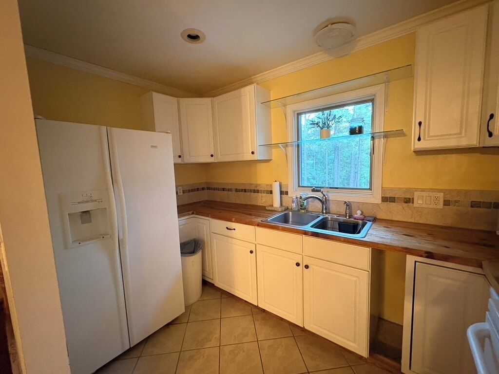Una cocina con armarios blancos, un lavamanos de acero inoxidable y un ventanal con vistas al verdor.