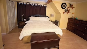 Une chambre à coucher comprenant un lit, une table de chevet, une commode, un ventilateur de plafond et une horloge murale.