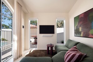 Ein modernes Wohnzimmer mit Fernseher, einem grünen Sofa, einem kleinen runden Tisch und einem großen abstrakten Gemälde.