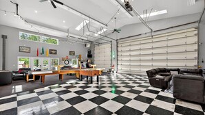 Una habitación amplia con piso a cuadros, una mesa grande, un sofá y una puerta de garaje.