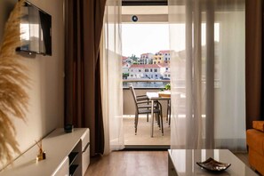Ein Balkon mit Esstisch und Stühlen, ein an der Wand befestigter Fernseher und Blick auf Gebäude über dem Wasser.