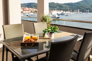 Ein Balkon mit Korbstühlen, einem Glastisch, Frühstücksgebäck und Topfpflanzen.