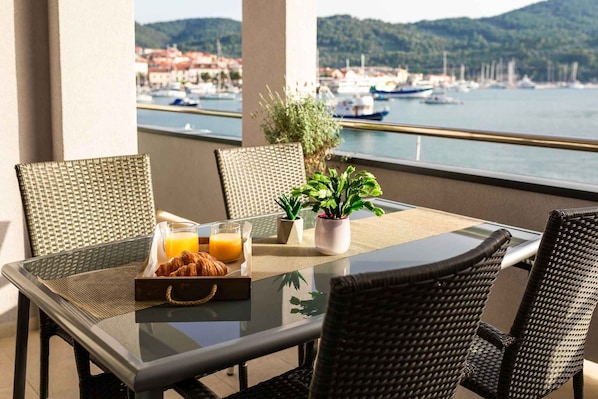 A balcony with wicker chairs, a glass table, breakfast items, and potted plants.