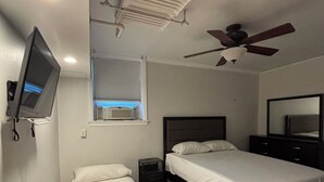 Een slaapkamer met twee bedden, een plafondventilator, een televisie en een raam met jaloezieën.