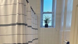 Een badkamer met toilet, wastafel, raam en plant, en een douchegordijn.