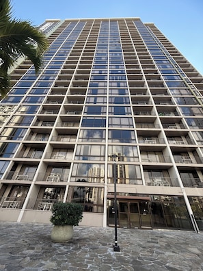Un edificio moderno e alto, con una facciata caratterizzata da un motivo a griglia di balconi, un ingresso in pietra e un cielo sereno.