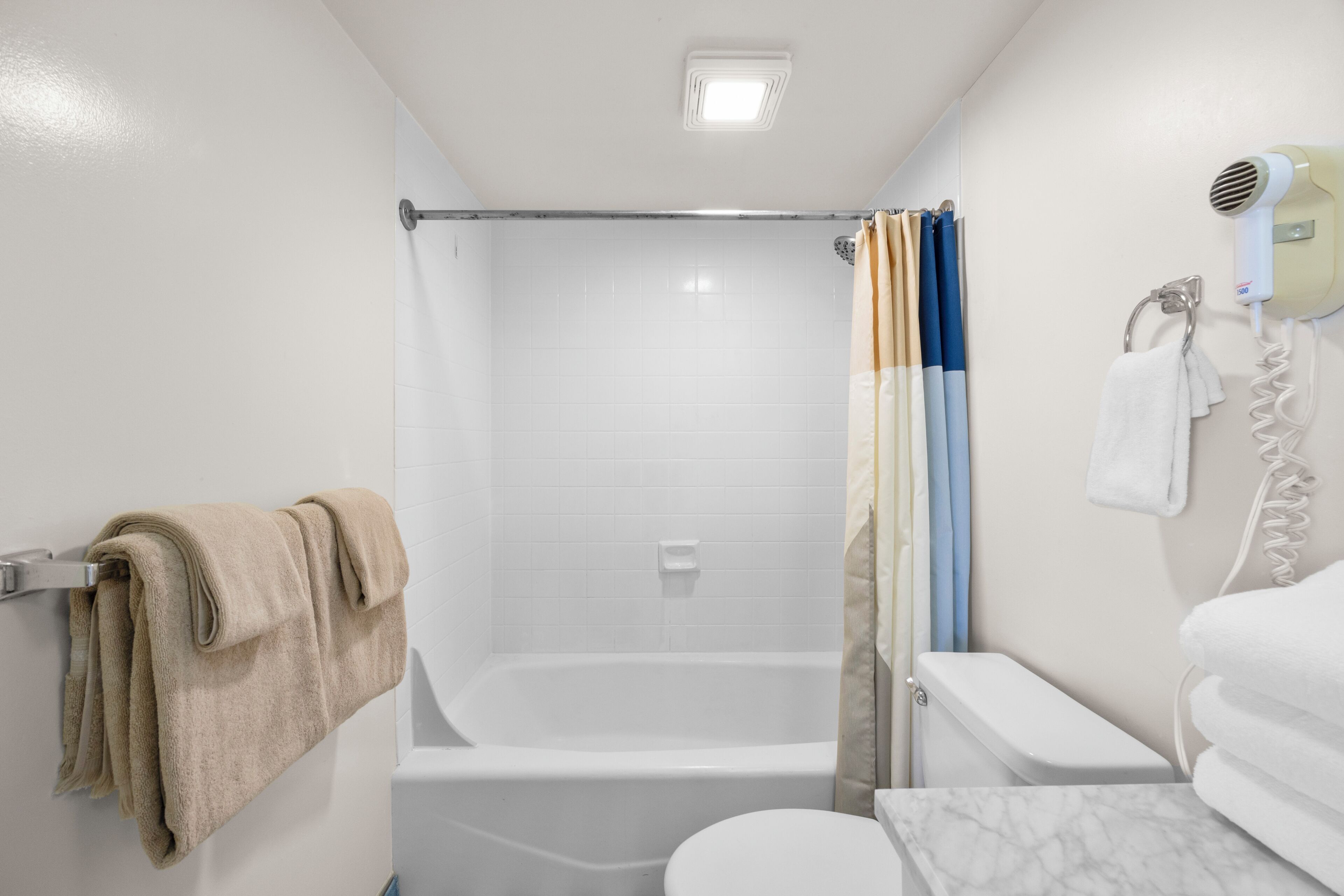 Une salle de bain équipée d’une baignoire, de toilettes et d’un sèche-cheveux fixé au mur.