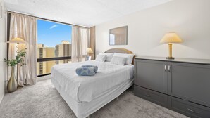 A hotel room with a large bed, a grey wardrobe, a city view, and a window with curtains. - Waikiki Cozy &Natural OceanMountain view hotel suite Free-parking  (Honolulu)