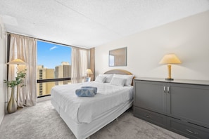Une chambre d’hôtel avec un grand lit, une armoire grise, une vue sur la ville et une fenêtre avec des rideaux.