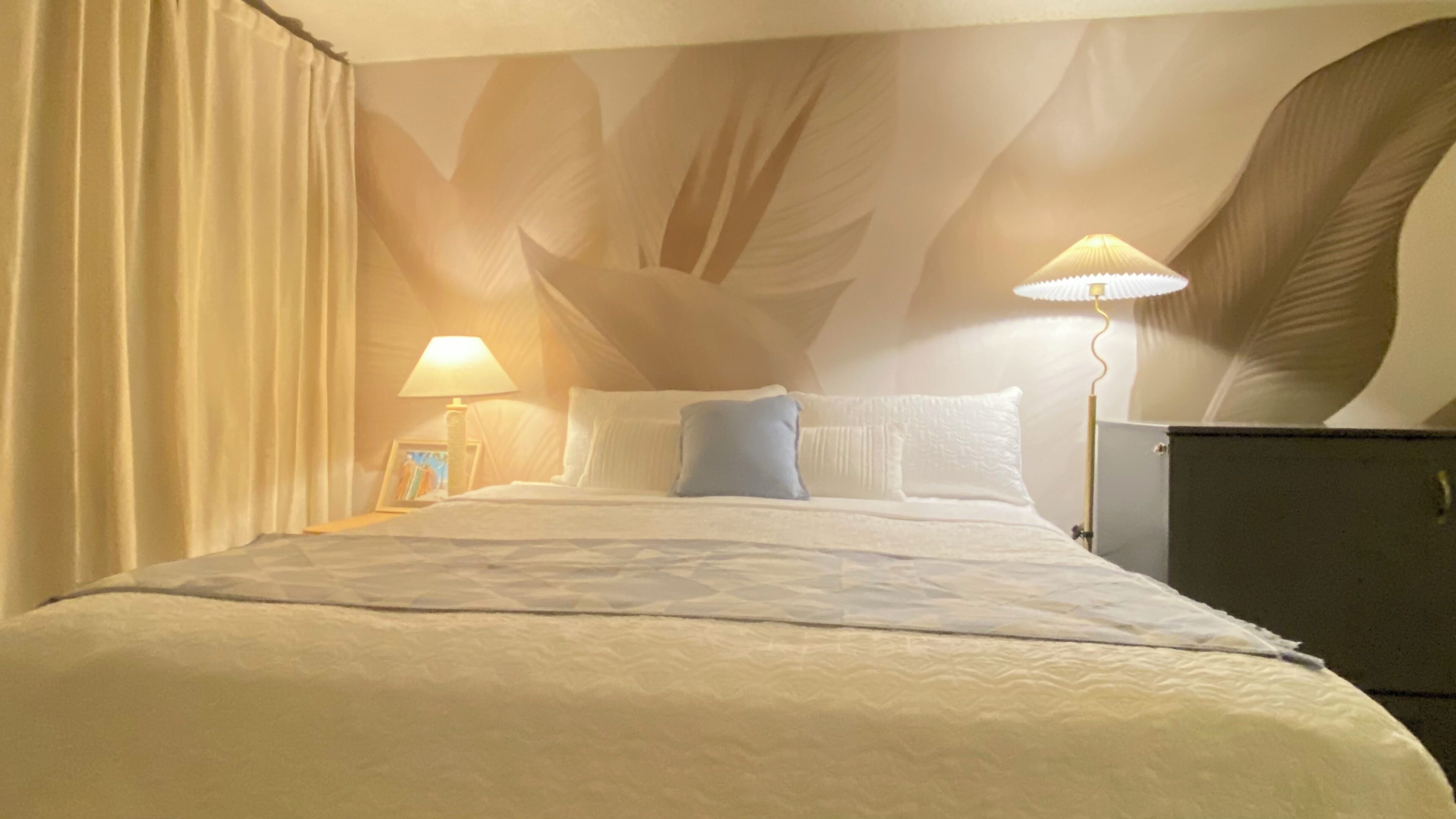 A hotel room with a bed, two bedside lamps, a nightstand, and a large wall mural.