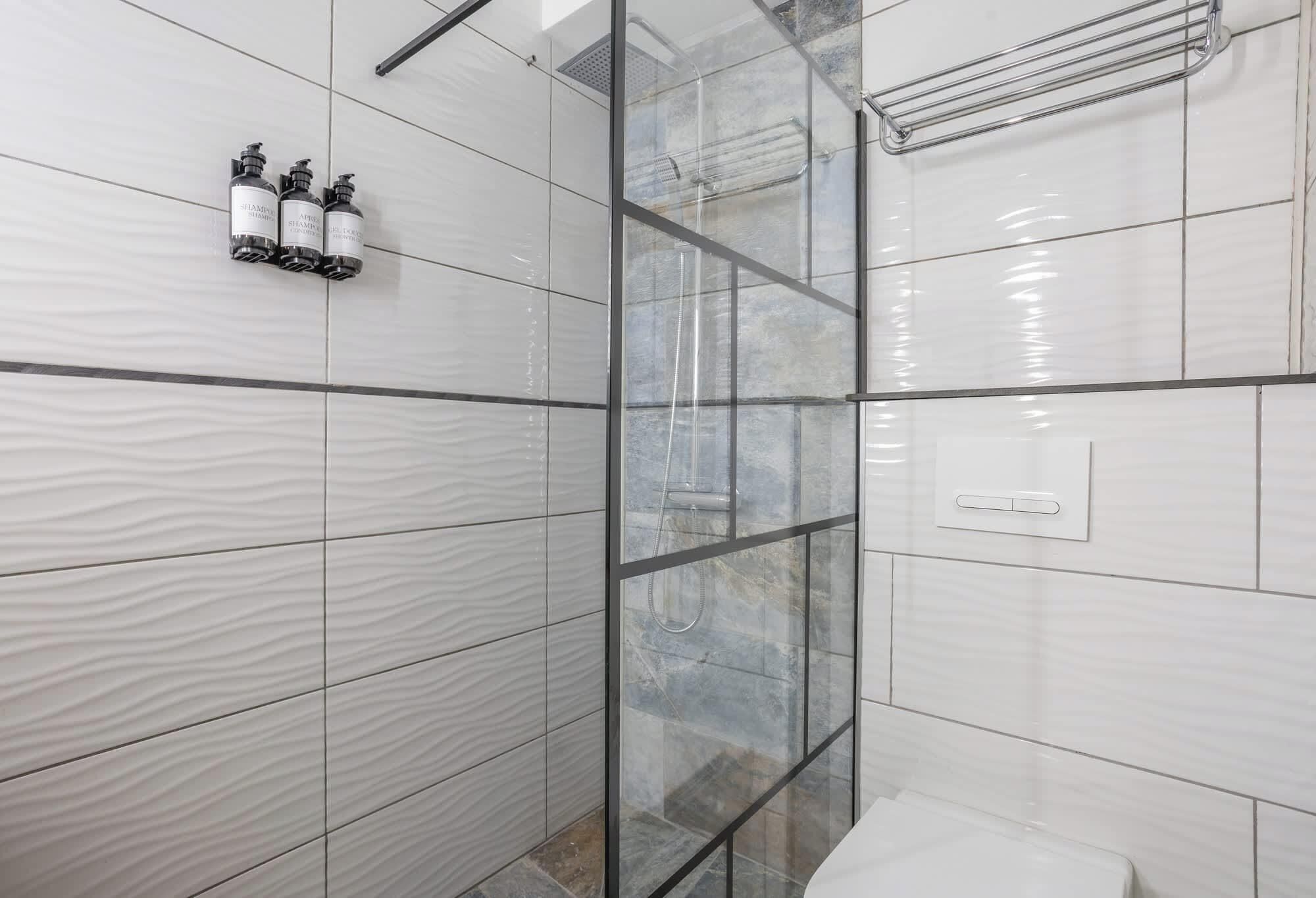 Une salle de bain moderne avec une douche à parois de verre, des carreaux blancs à texture et des toilettes.