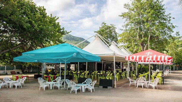 A covered outdoor seating area with tables and chairs, a tent structure, and a red umbrella. - 2BR Apartment Planteur - Beachfront (Les Trois-Îlets)