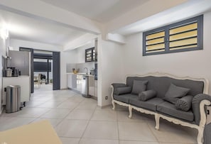 Ein modernes Wohnzimmer mit grauem Sofa, einer weißen Akzentwand und einer Küche im Hintergrund.