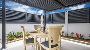 A covered patio with a table set for four, surrounded by chairs, under a metal roof structure. - 2BR Apartment Planteur - Beachfront (Les Trois-Îlets)