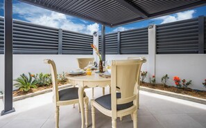 Eine überdachte Terrasse mit Tisch und Stühlen für vier Personen, unter einer Metallkonstruktion.