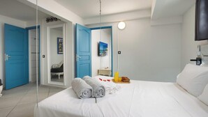 A hotel room with a bed, a TV, a door, and a mirror. - 2BR Apartment Planteur - Beachfront (Les Trois-Îlets)