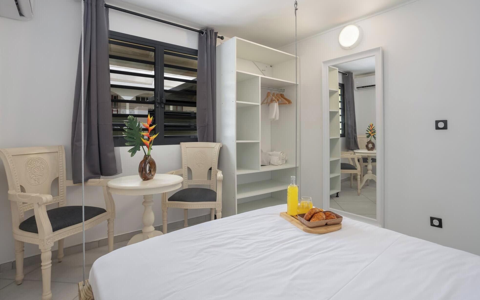 Une chambre d’hôtel comprenant un lit, deux chaises, une petite table, une armoire et un miroir.