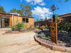 A wooden building with a wooden deck, a garden with flowers, and a wooden sign with text.