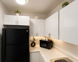 Eine moderne Küche mit weißen Schränken, einem schwarzen Kühlschrank, einer Mikrowelle und einem Spülbecken.