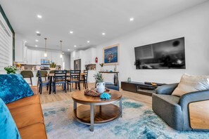Un salon moderne avec une table basse ronde, un canapé, un coin repas avec des chaises et une cuisine en arrière-plan.