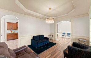 A spacious living room with a blue sofa, a chandelier, and a view to a dining area. - Pet-Friendly Loganville Retreat • Near Parks (Loganville)