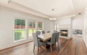 A dining area with a wooden table and chairs, a fireplace, and large windows with blinds. - Pet-Friendly Loganville Retreat • Near Parks (Loganville)