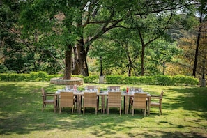 Un espace de restauration en plein air, avec des tables et des chaises en osier, entouré d’une végétation luxuriante et d’arbres.