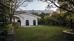 Un edificio blanco con entradas arqueadas, rodeado de un césped cuidado y árboles, con montañas al fondo.