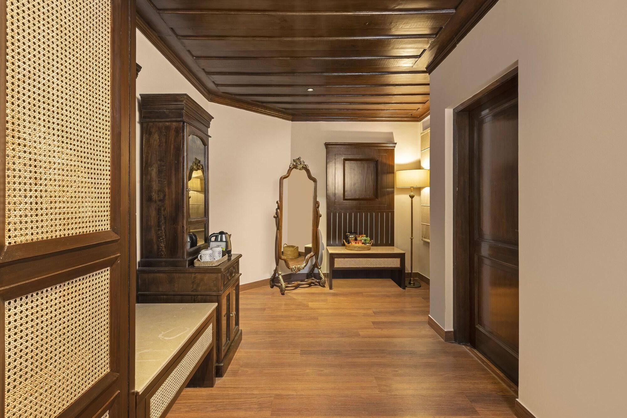 A hallway with wooden flooring, a mirror, a bench, and a lamp.