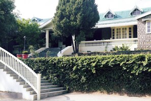 A building with a staircase leading to a covered area, surrounded by greenery. - Brij Anayra Dharamshala (Dharamshala)