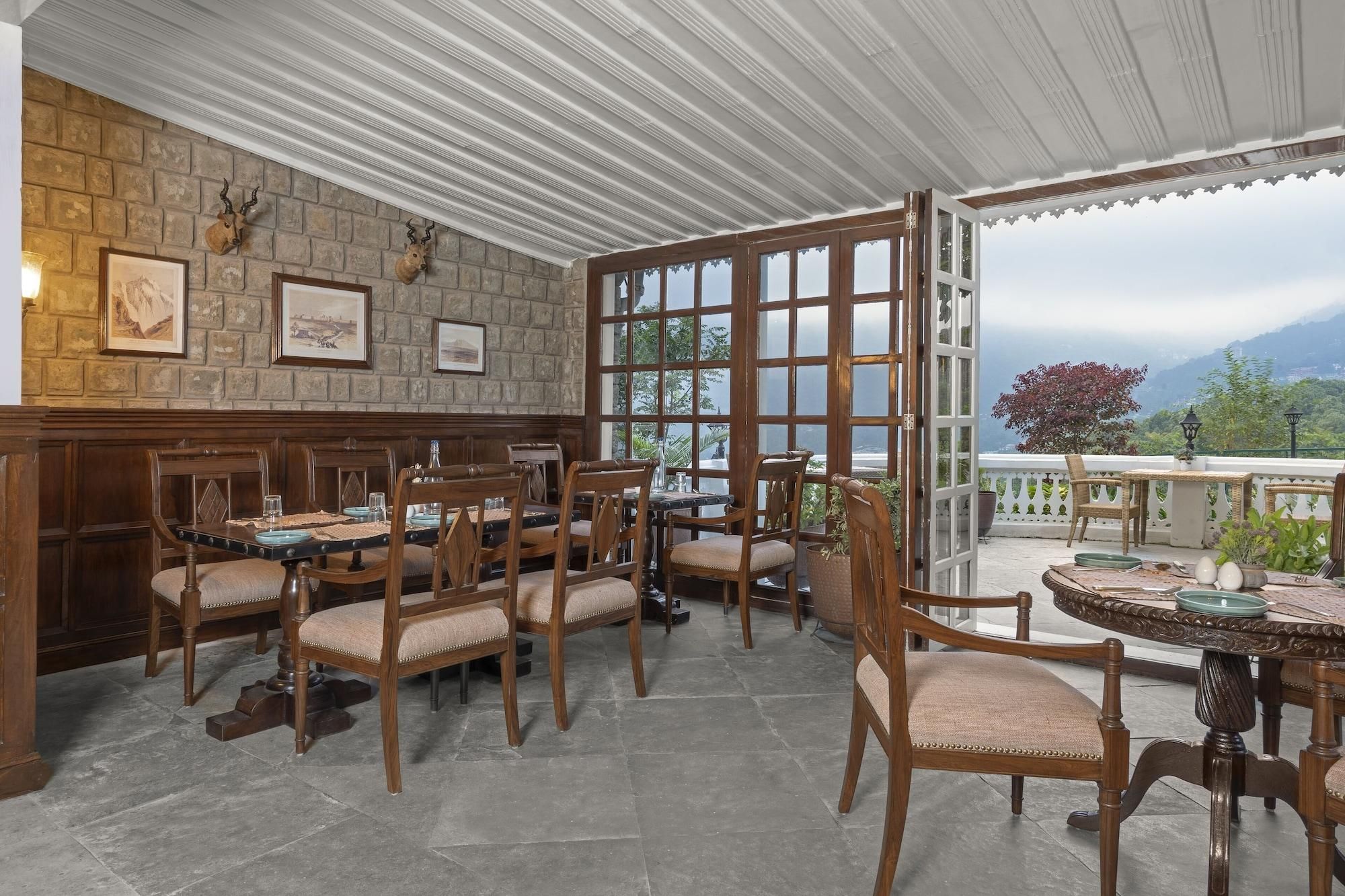 A restaurant with a stone wall, wooden chairs, a bar, and large windows offering a mountain view.