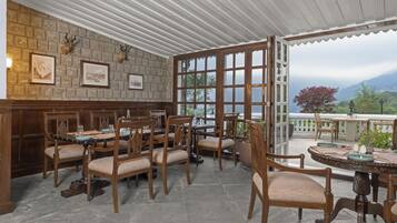A restaurant with a stone wall, wooden chairs, a bar, and large windows offering a mountain view.