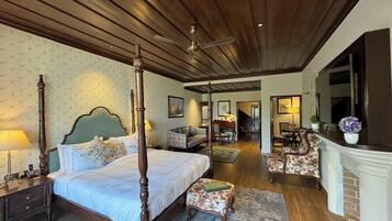 A four-poster bed with a nightstand, a small table with a lamp, a chair, and a fireplace.