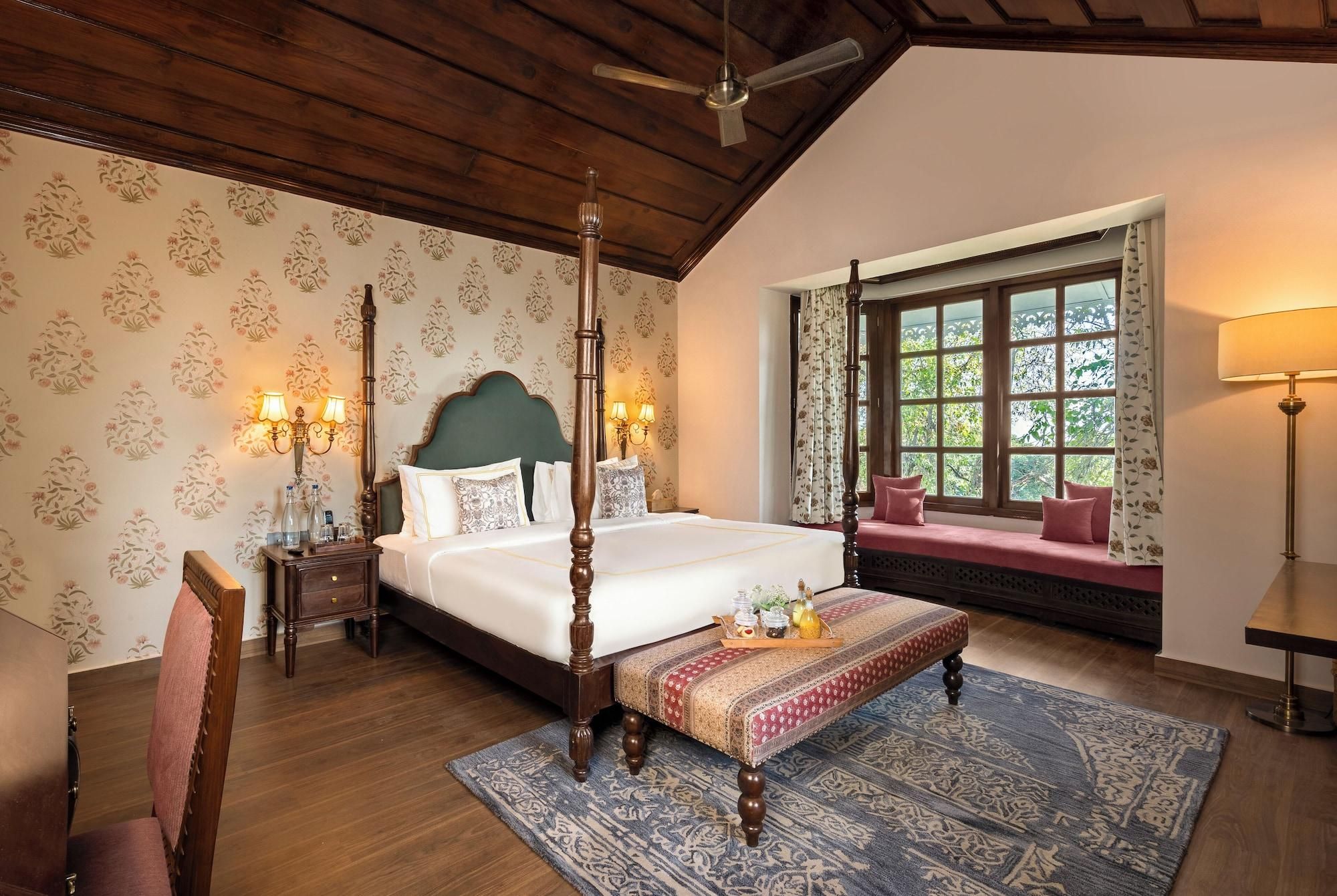 A bedroom with a four-poster bed, a bench, a window with a view, and a ceiling fan.