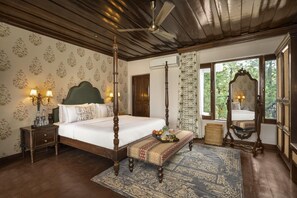 A four-poster bed with a wooden headboard, a bedside table with a lamp, a bench with a tray of fruit, and a large mirror. - Brij Anayra Dharamshala (Dharamshala)