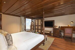 A bedroom with a large bed, a wooden ceiling, a desk with a lamp, and a view of the sky. - Brij Anayra Dharamshala (Dharamshala)