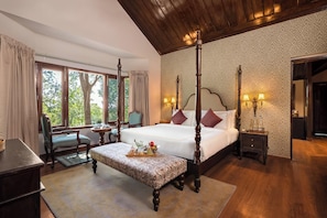 A four-poster bed with a wooden headboard, a bedside table with a lamp, a chair, and a small table with a tray of toiletries. - Brij Anayra Dharamshala (Dharamshala)