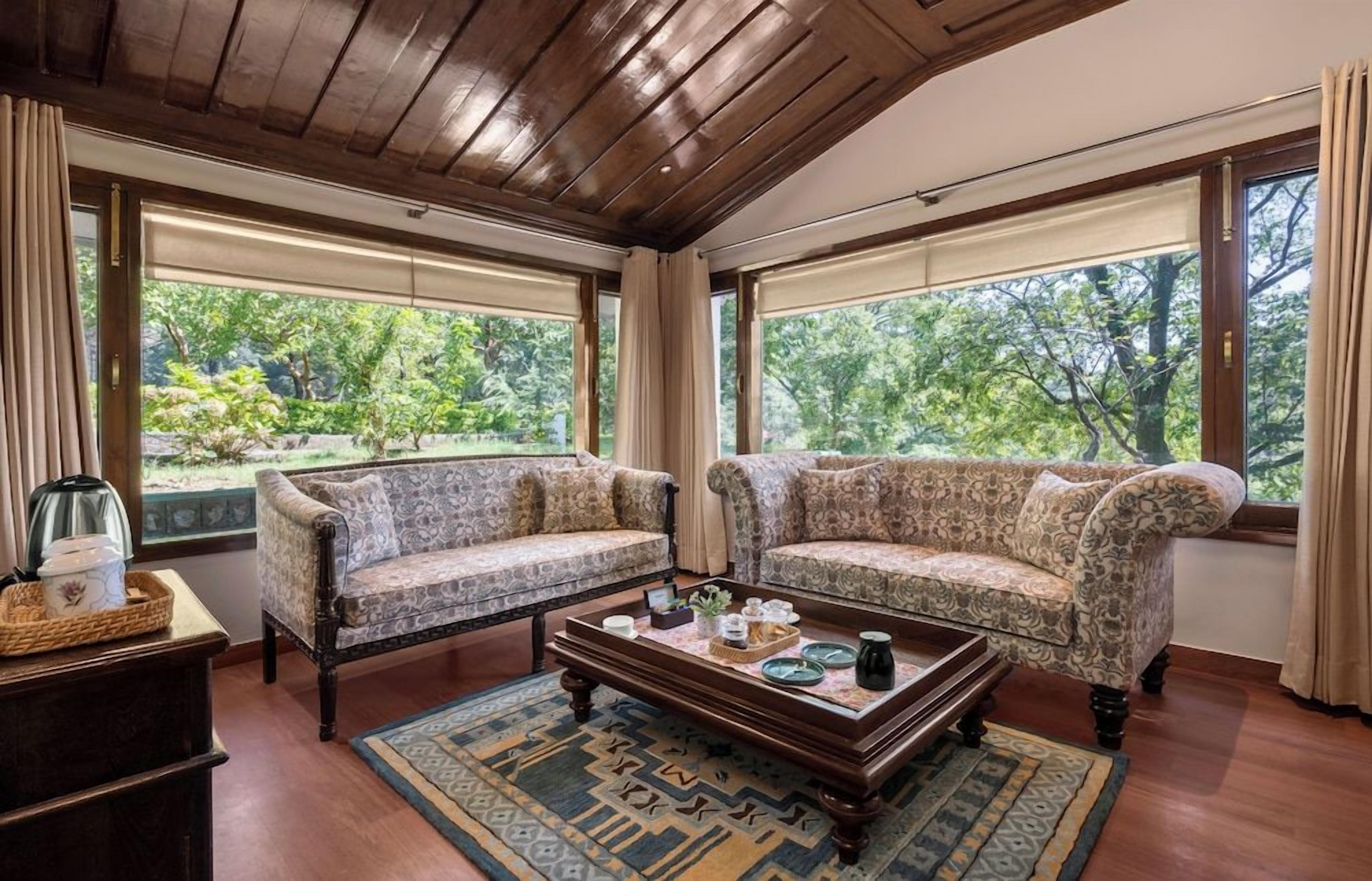 A room with two patterned sofas, a wooden coffee table, and a view of greenery through large windows.