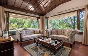 A room with two patterned sofas, a wooden coffee table, and a view of greenery through large windows.