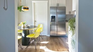 Una cuina moderna amb nevera d'acer inoxidable, sòl de fusta i zona de menjador amb cadires grogues.