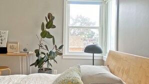 Un dormitori amb un llit, una finestra, un escriptori i una planta en test.