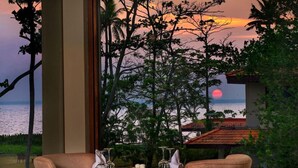 A dining area with a table set for two, overlooking a sunset view with trees and a body of water. - Niraamaya Retreats Backwaters and Beyond, Kumarakom (Kottayam)