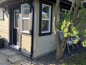 Een huis met een voordeur, twee ramen, een boom en tuinmeubilair.
