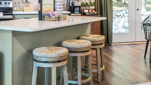 A kitchen with a bar area, wooden stools, a coffee machine, and a framed book on the counter.
