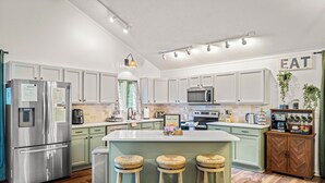 A modern kitchen with stainless steel appliances, a central island with stools, and a 'EAT' sign on the wall.